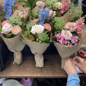 Florist tying hessian-wrapped flower bouquets at a wooden bench